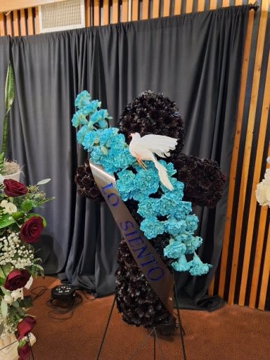 Standing floral tribute with blue flowers, dark blooms, and a white dove