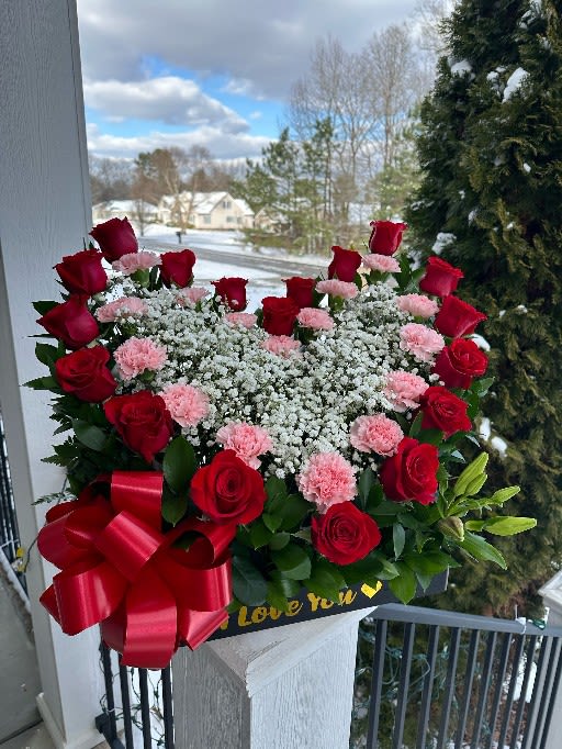 Heart-shaped bouquet of red roses and pink carnations with a red ribbon