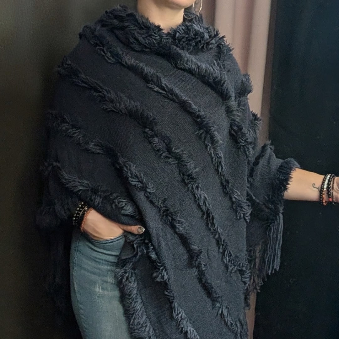Person wearing a black fringed poncho and jeans