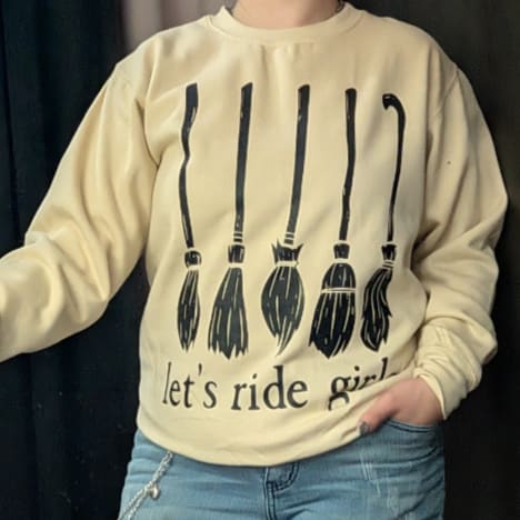Person wearing a beige sweatshirt with black broom graphics and text