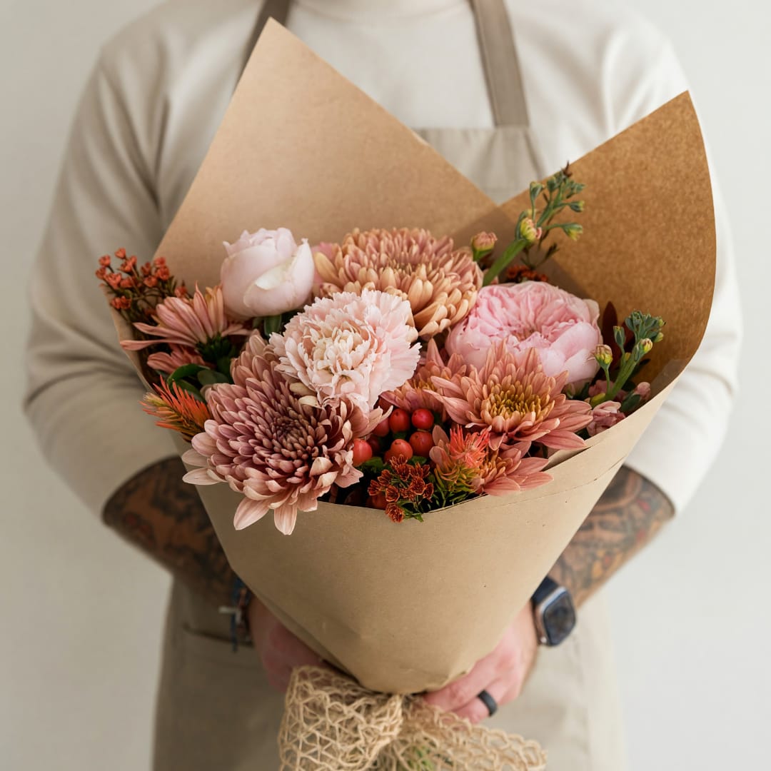 Handheld bouquet of pink and peach flowers wrapped in brown paper