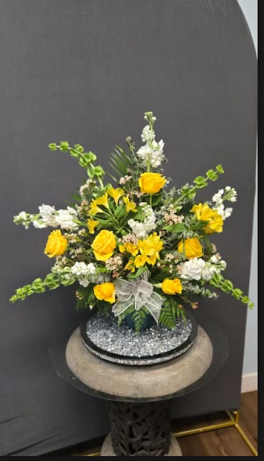 Yellow and White Sympathy Floor basket - Sunlit yellow roses paired with crisp white spiked stock create a graceful sympathy floor basket designed to comfort and uplift. This yellow and white sympathy floor basket reads as both respectful and hopeful-the kind of arrangement that quietly brightens a service or memorial while conveying sincere condolences.  The design spreads outward in a full, layered composition with arching stems and clusters of small filler blooms for texture and movement. Roses, alstroemeria, stock, and other seasonal white and green accents are arranged in a round container finished with decorative sheer ribbon bow for a polished, gentle touch.   Perfect for funerals, memorial services, or to send comfort to the person you're thinking of, this basket offers a balanced visual presence that won't overwhelm the space. Sized for floor display, it arrives ready to place and enjoy; standard floral care-keeping water fresh and away from direct heat-helps preserve the blooms for as long as possible.