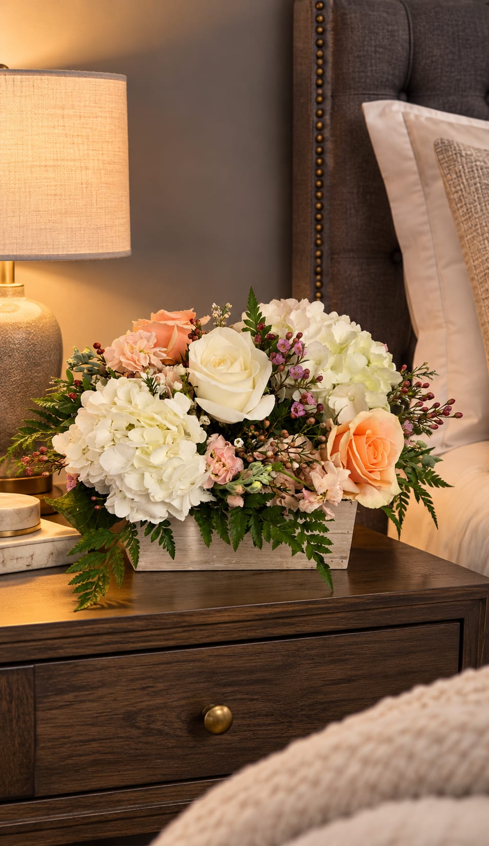 Cream and peach floral arrangement in a white wooden box on a bedside table