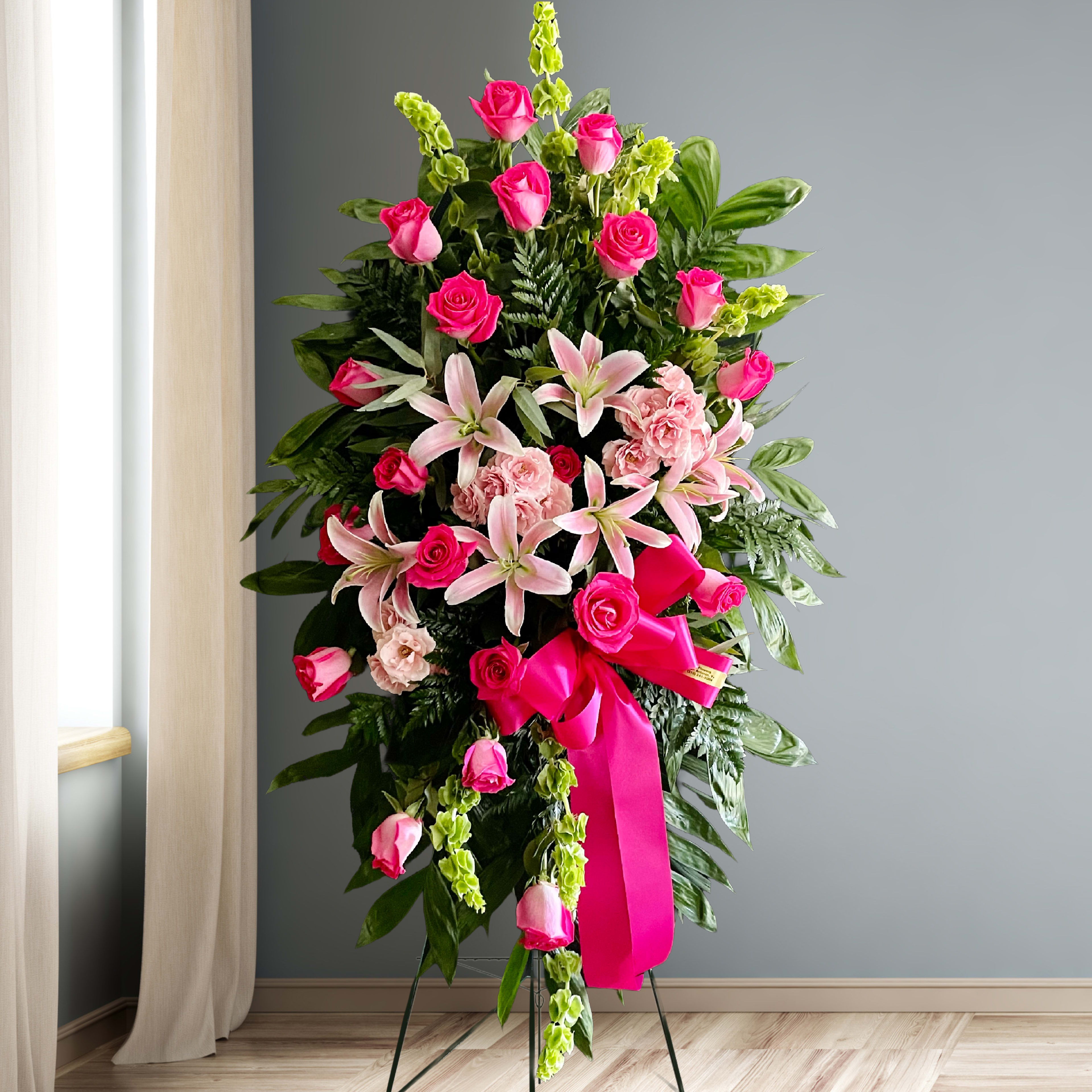 Tall standing floral spray with pink roses and lilies on a ribboned easel