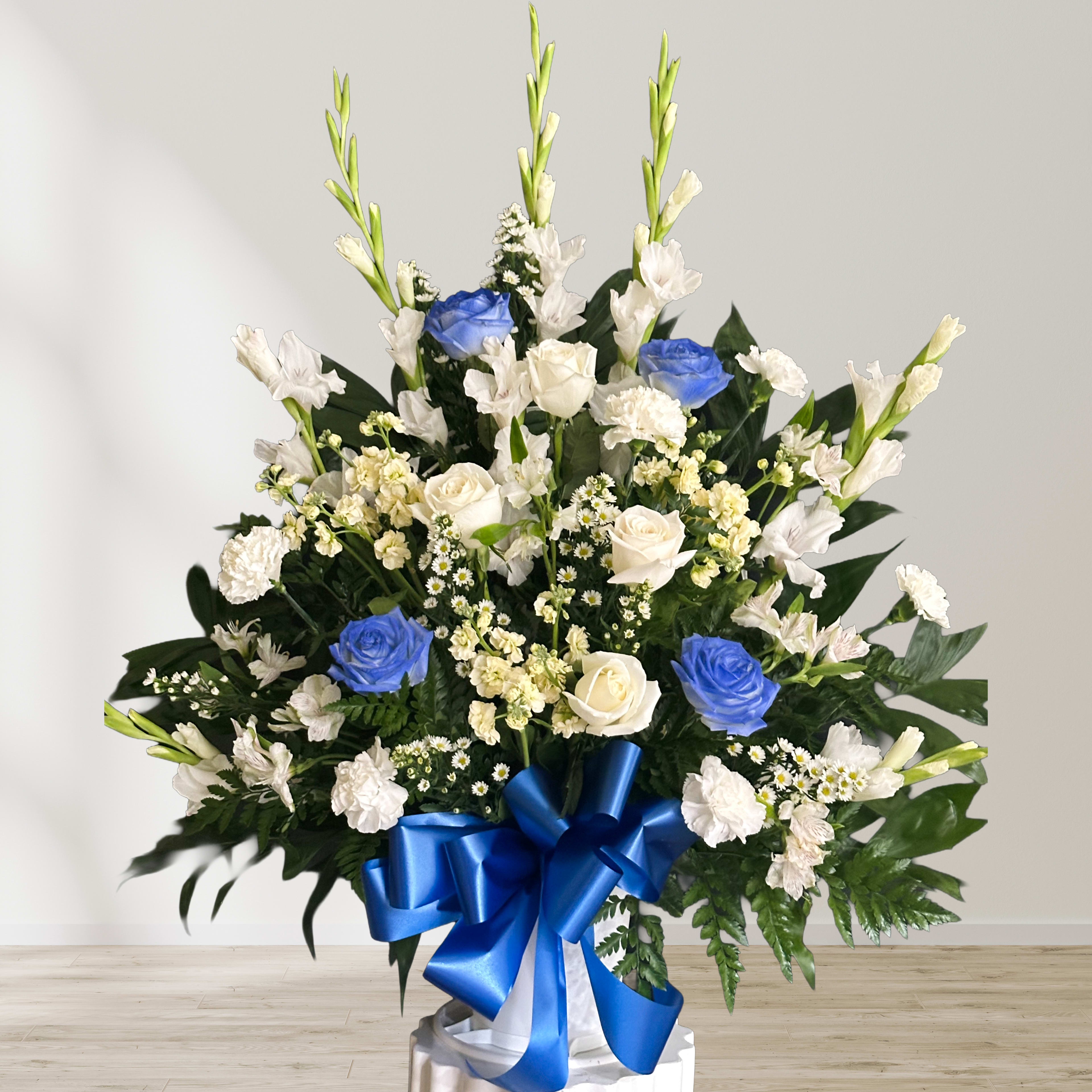 Large white and blue floral arrangement with a blue ribbon on a pedestal