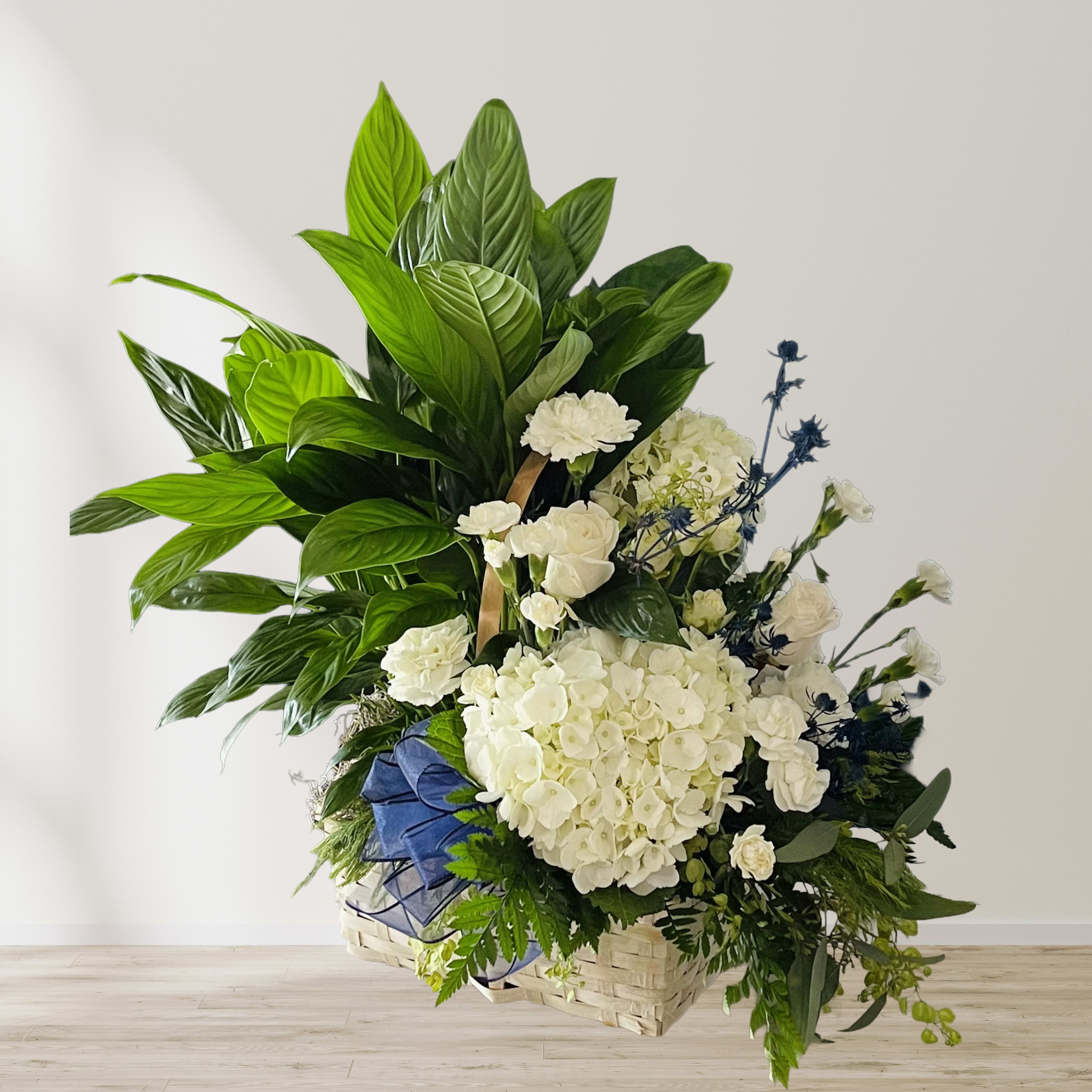 Large white floral arrangement with green foliage in a woven basket