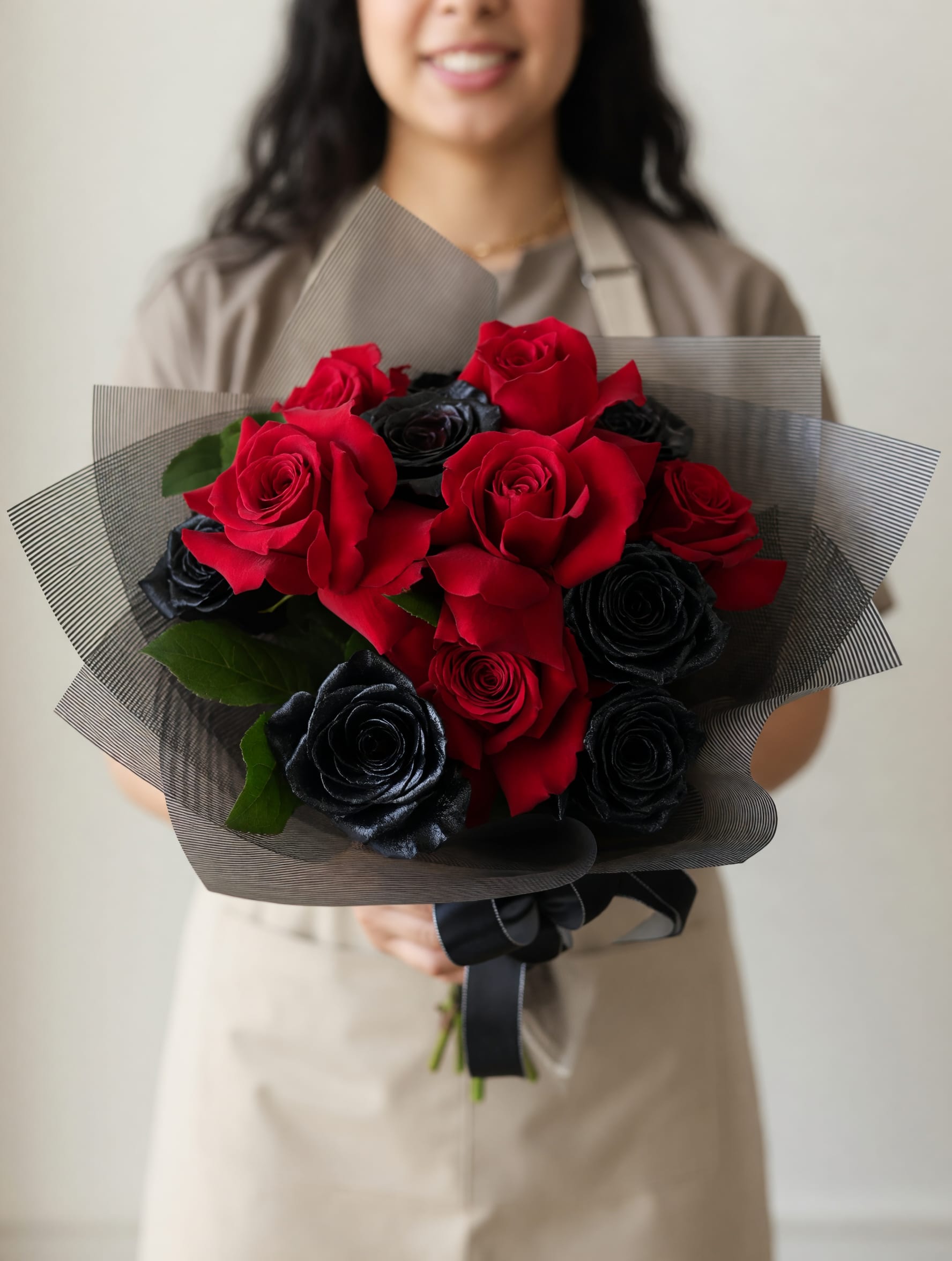 Dark Matter - Dark Matter is a Halloween‑inspired flower arrangement that reads like a moody, modern statement piece - a compact bouquet of roses designed for birthday surprises, graduation celebrations, thank-you gestures, or a bold just-because moment. The dramatic contrast between saturated red roses and black‑dyed roses creates an intense, high‑impact look that will make the person you're thinking of feel seen, desired, and a little spellbound.  This arrangement features a dense cluster of roses wrapped in layered dark gray and black wrapping paper and finished with black wrapping paper accents and a glossy black ribbon. Small green leaves peek through the blooms to add depth against the red and black palette; the compact, tightly packed construction highlights the velvety texture of each rose. Hard goods include decorative wrap and ribbon that keep the bouquet sleek and ready to present.  Perfect for a Halloween‑tinged birthday, a graduation gift with attitude, or a dramatic thank-you that won't go unnoticed, Dark Matter is the kind of bouquet that reads intentionally romantic and daring. The bouquet arrives wrapped and ready to gift for delivery in San Antonio, TX; to care for the roses, place stems in fresh water and keep them out of direct sun to extend vase life.