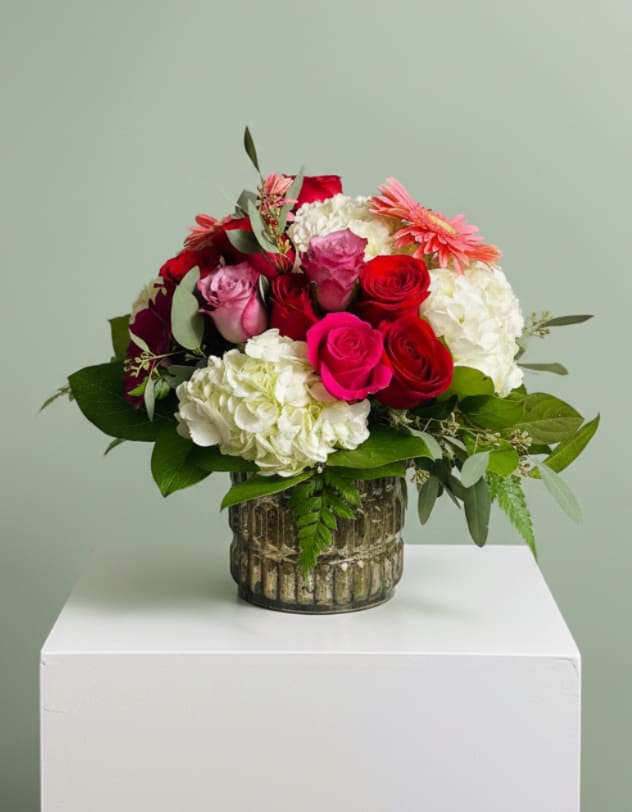 Timeless Love - Celebrate Mom with a design that speaks of love, admiration, and timeless beauty. Timeless Love for Mom features a luxurious blend of rich red and vibrant pink roses, nestled among soft, cloud-like hydrangea and accented with fresh greenery for a full, elegant look.  Arranged in a beautifully textured keepsake vase, this piece offers a classic yet elevated style—perfect for making her feel truly special. The combination of bold and soft tones creates a romantic, balanced design that stands out while still feeling warm and heartfelt.  Each arrangement is handcrafted and uniquely designed, ensuring no two are exactly alike—just like every mother’s love. Includes a personalized card message so you can share your appreciation in your own words.  Custom requests are always welcome—we’re here to help you create the perfect gift for Mom this Mother’s Day. 