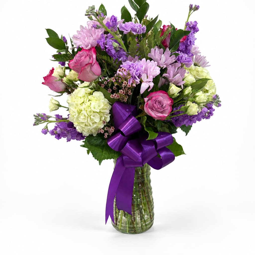 Bouquet of pink, purple, and white flowers in a glass vase with a purple ribbon