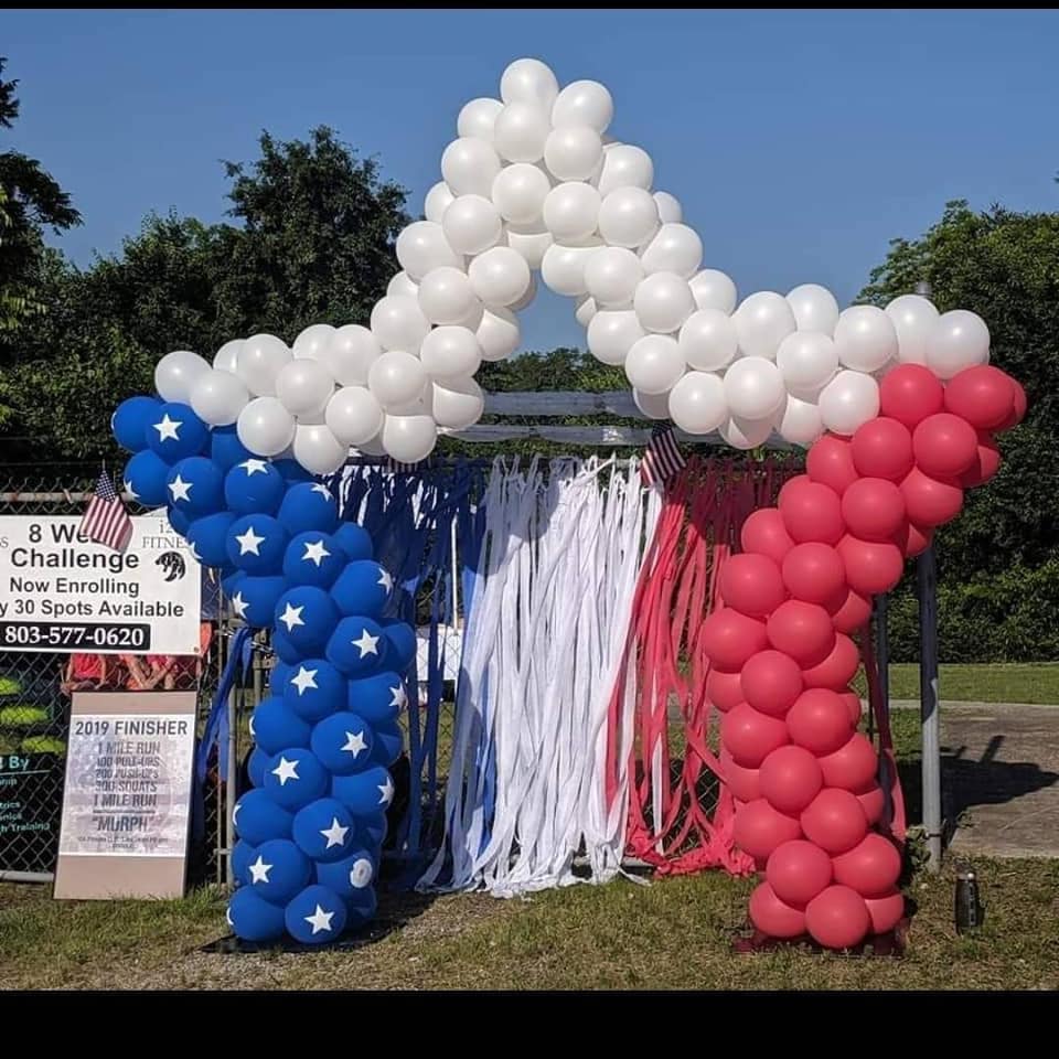 Red, white, and blue balloon arch with hanging streamers outdoors