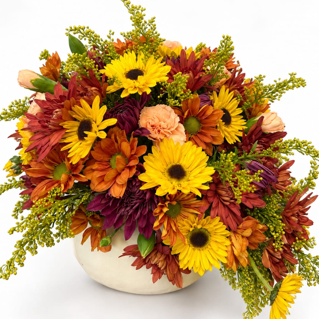 Mixed bouquet of yellow, orange, and burgundy flowers in a cream vase