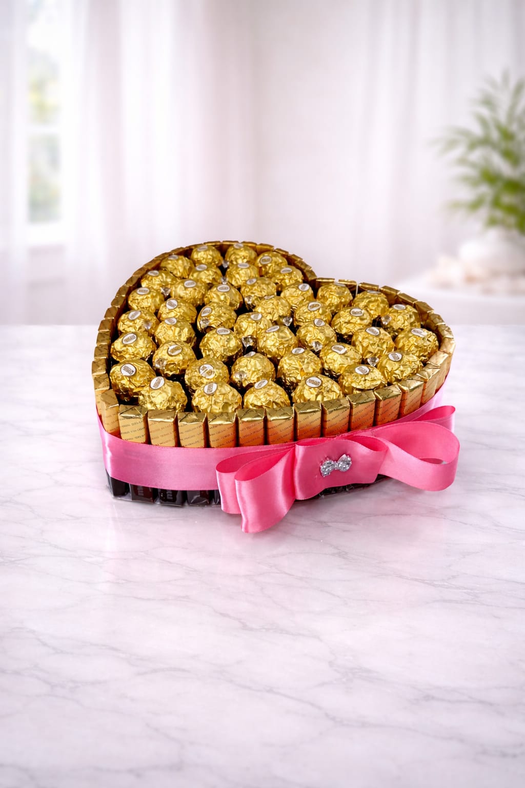 Heart-shaped arrangement of gold-wrapped chocolates with a pink ribbon bow