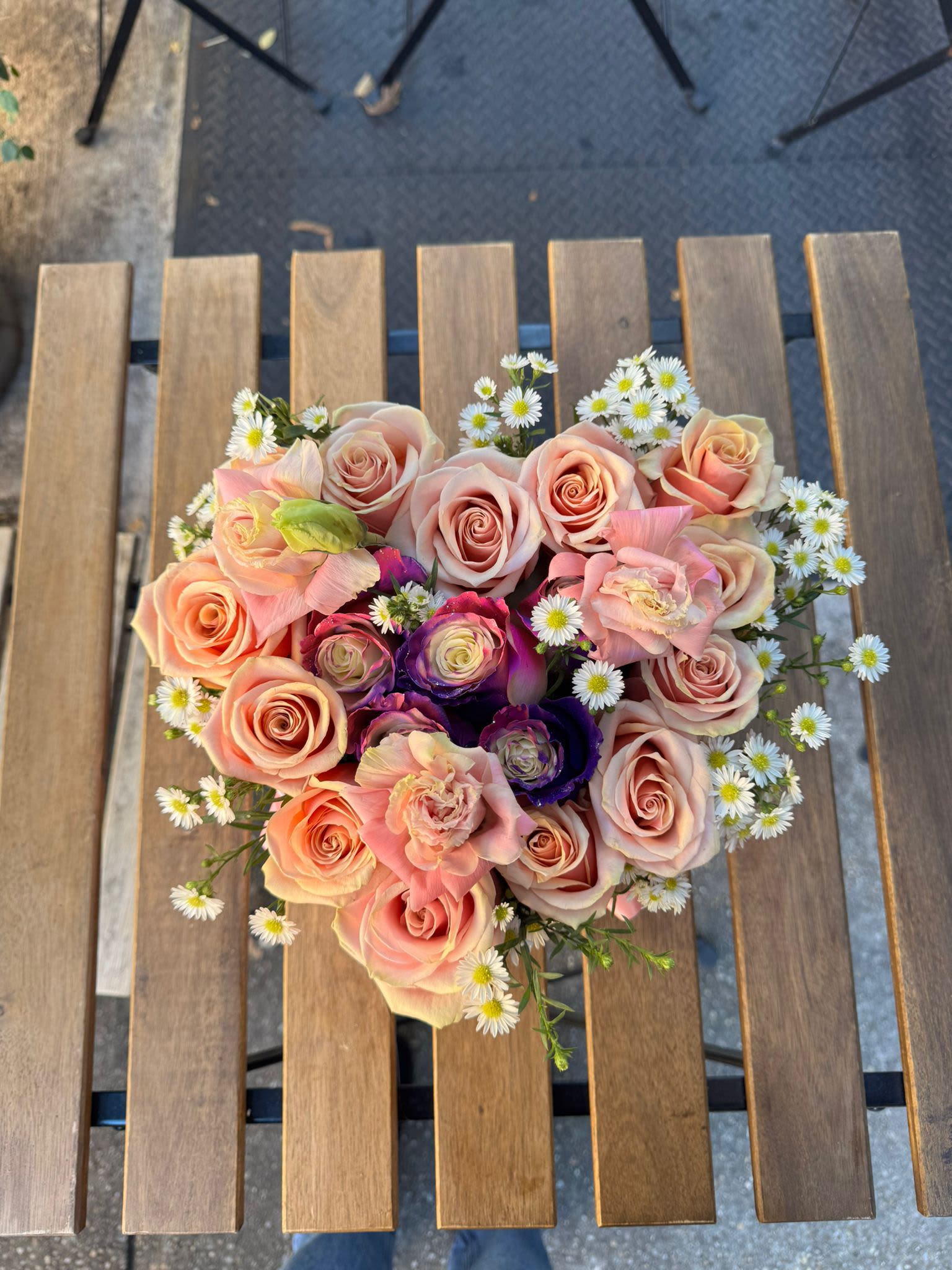 Heart-shaped bouquet of pink and peach roses with small white daisies
