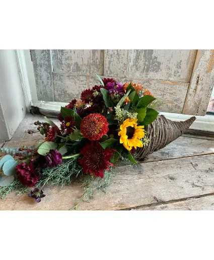 Contemporary Horn of Plenty - Made with natural materials this beautiful cornucopia arrangement features mums, gerbera daisies, carnation and sunflowers.  Includes: Mums, Carnations, Gerbera Daisy, Sunflowers And Seasonal Foliage In Cornucopia.