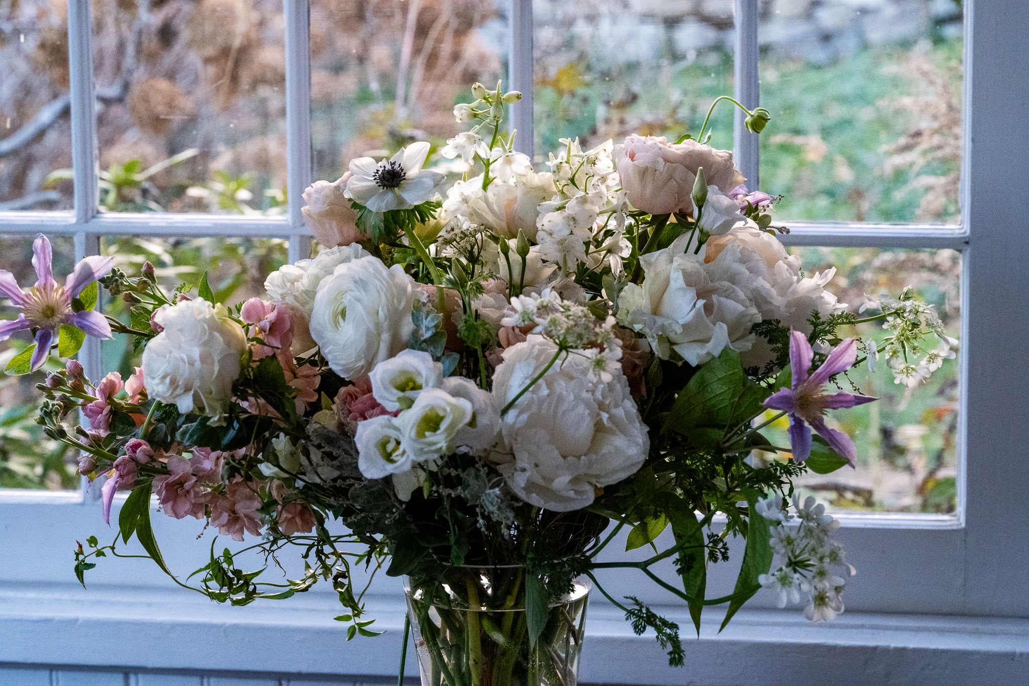 Spring Bounty - A spring garden medley of beautiful premium flowers including peonies and cloni ranunculus.  A stunning tall display that will enhance a foyer or any focal point in the home.  Soft peach, cream and whites with touches of lavender further enhance this beautiful bouquet.  