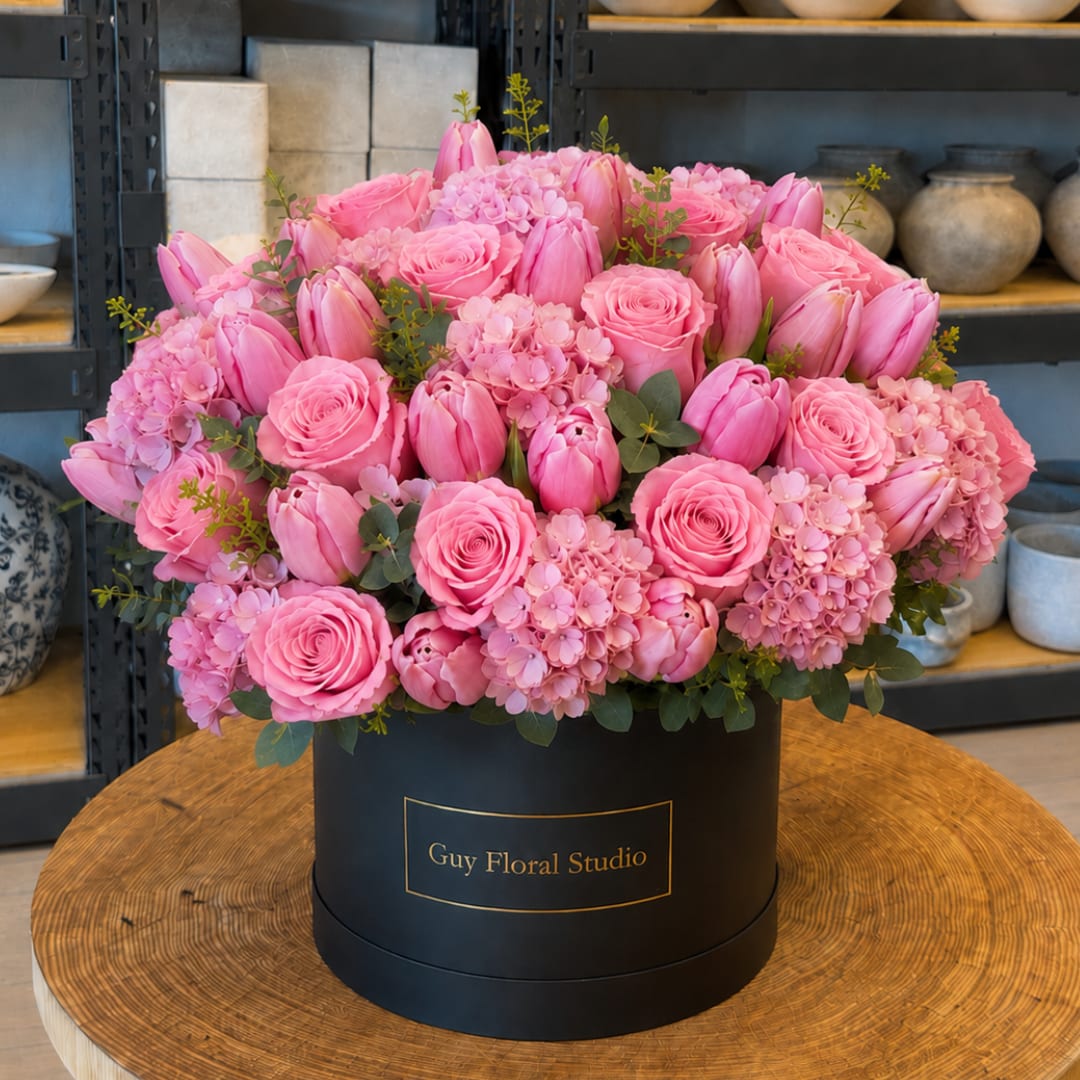 Pink roses and tulips arranged in a black round box