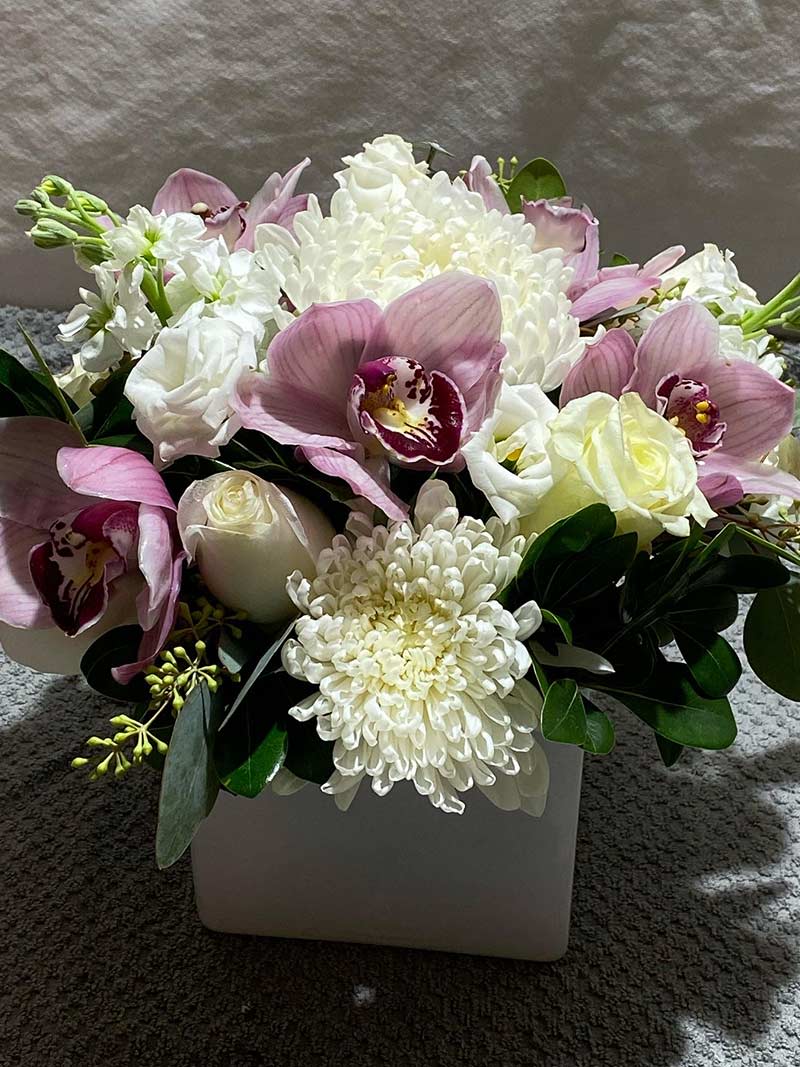 Pink orchids and white chrysanthemums in a square white vase