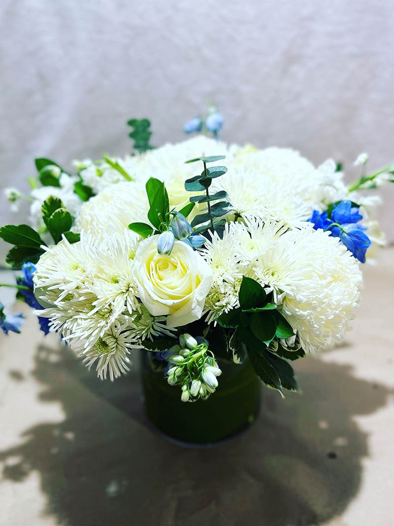White and blue floral arrangement in a dark vase