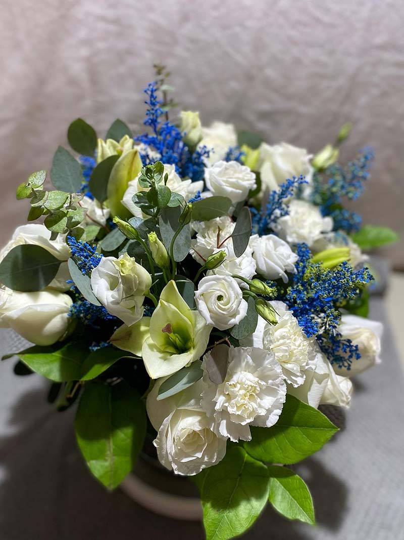 White bouquet with blue accents and green foliage in a vase
