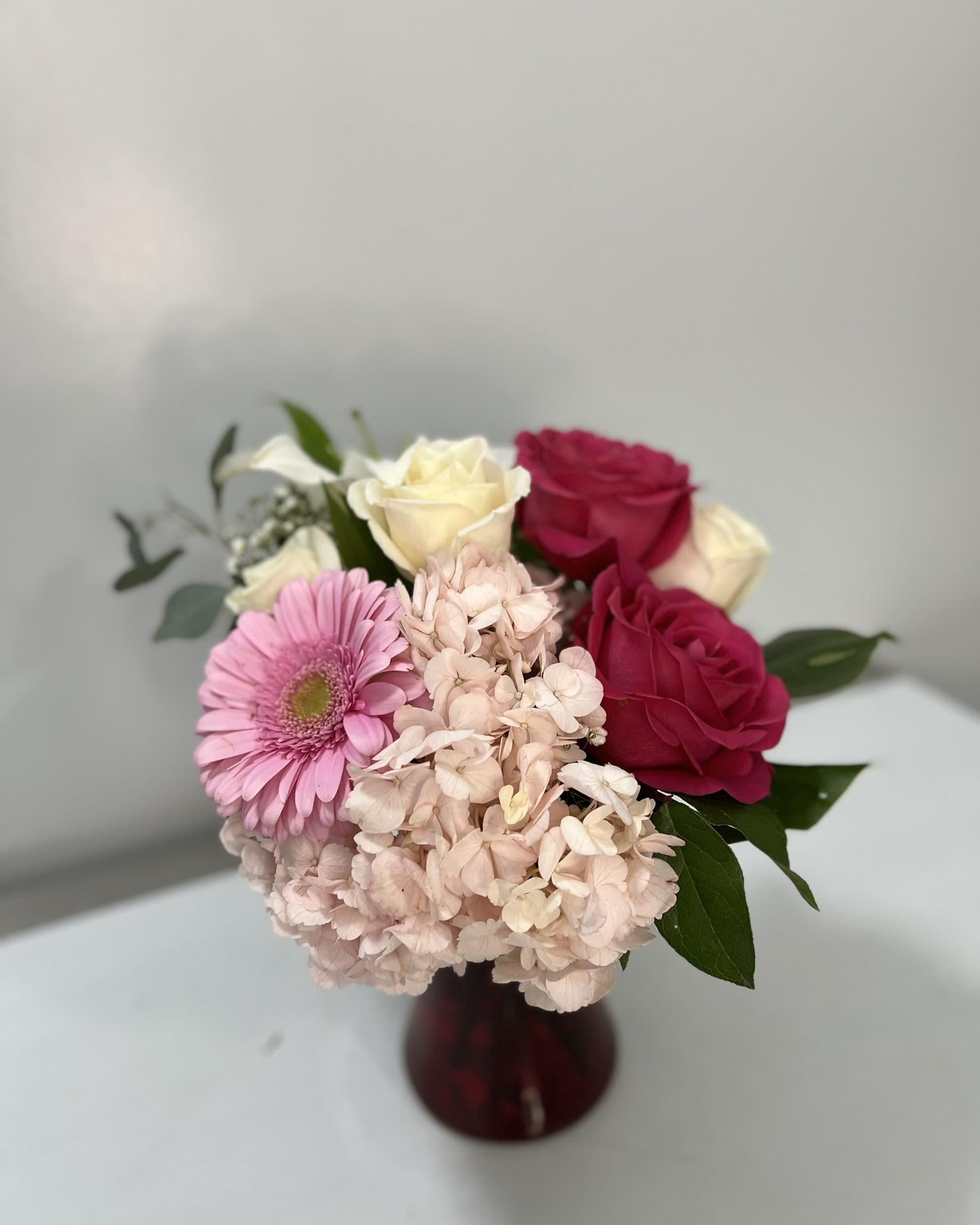 Pink and white bouquet with roses and hydrangeas in a burgundy vase