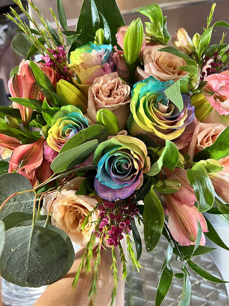 Bouquet of rainbow-dyed roses with pink lilies and greenery