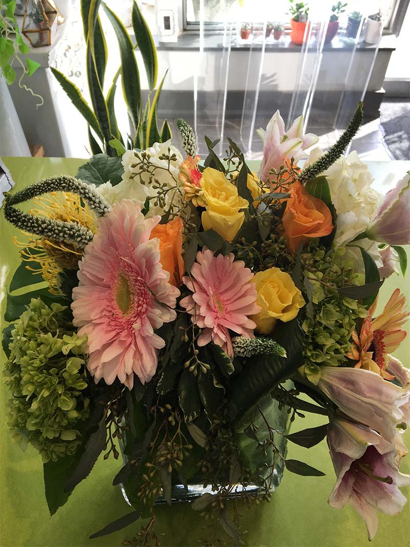 Mixed bouquet with pink gerberas, yellow and peach roses, and lilies in a glass vase