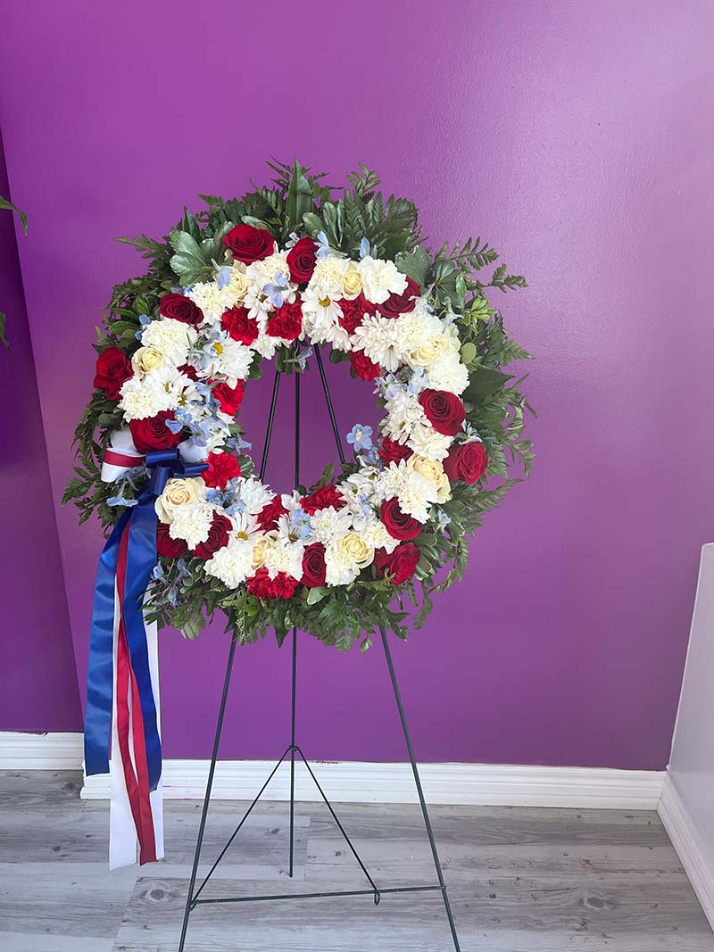 Circular floral wreath on a stand with red, white, and blue flowers