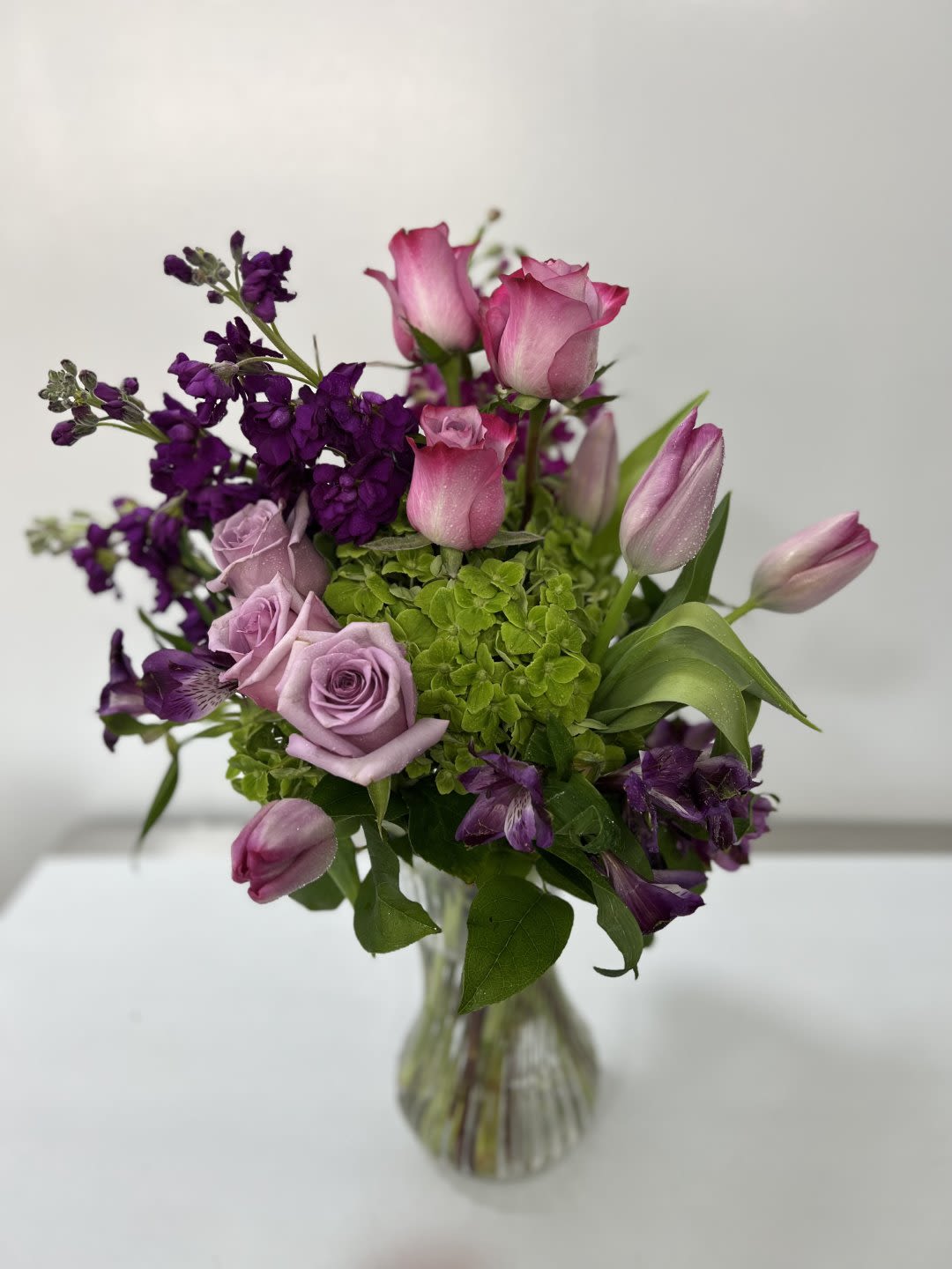 Pink roses and tulips with purple flowers in a glass vase