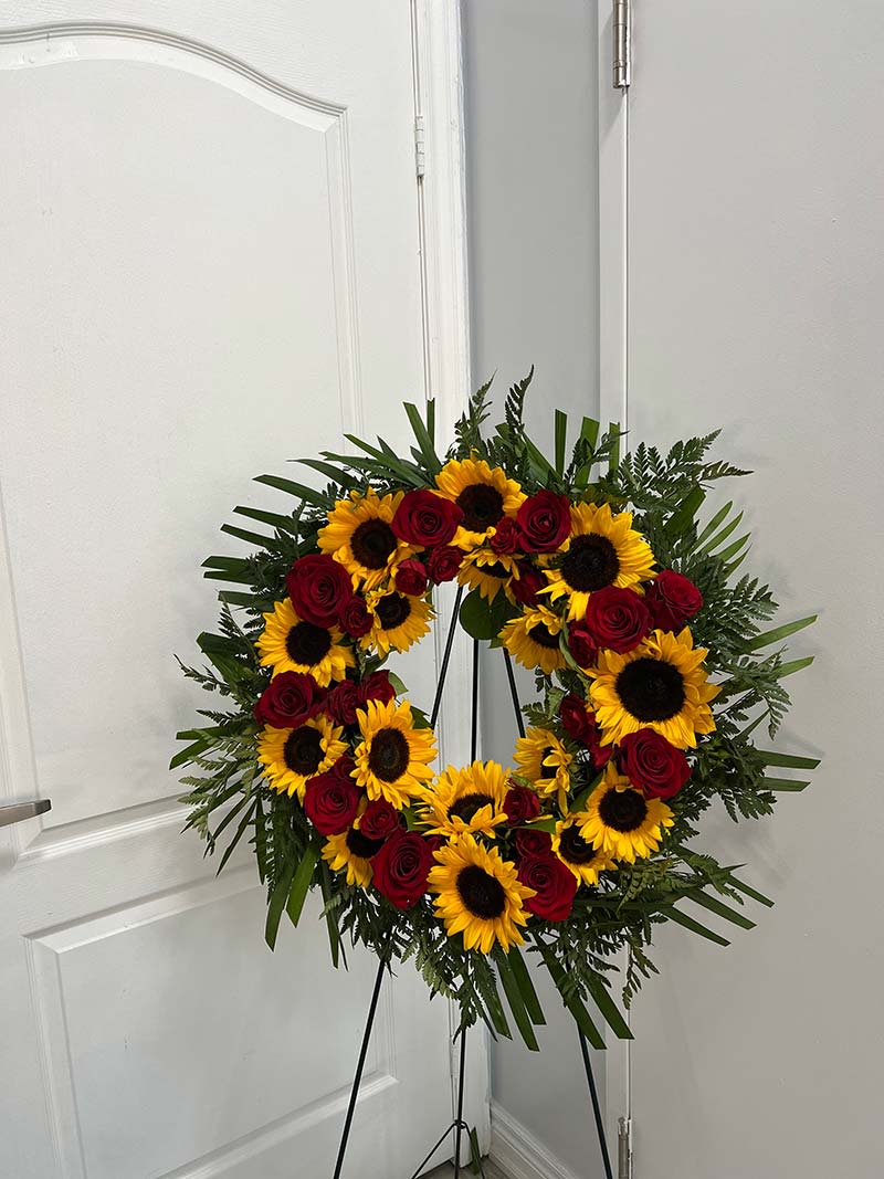 Circular wreath of red roses and yellow sunflowers on a stand