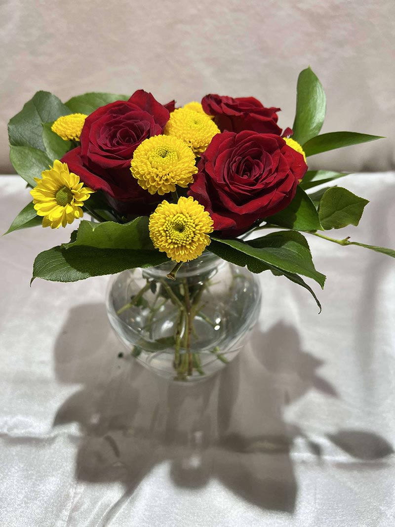 Red roses and yellow pom flowers in a clear glass vase