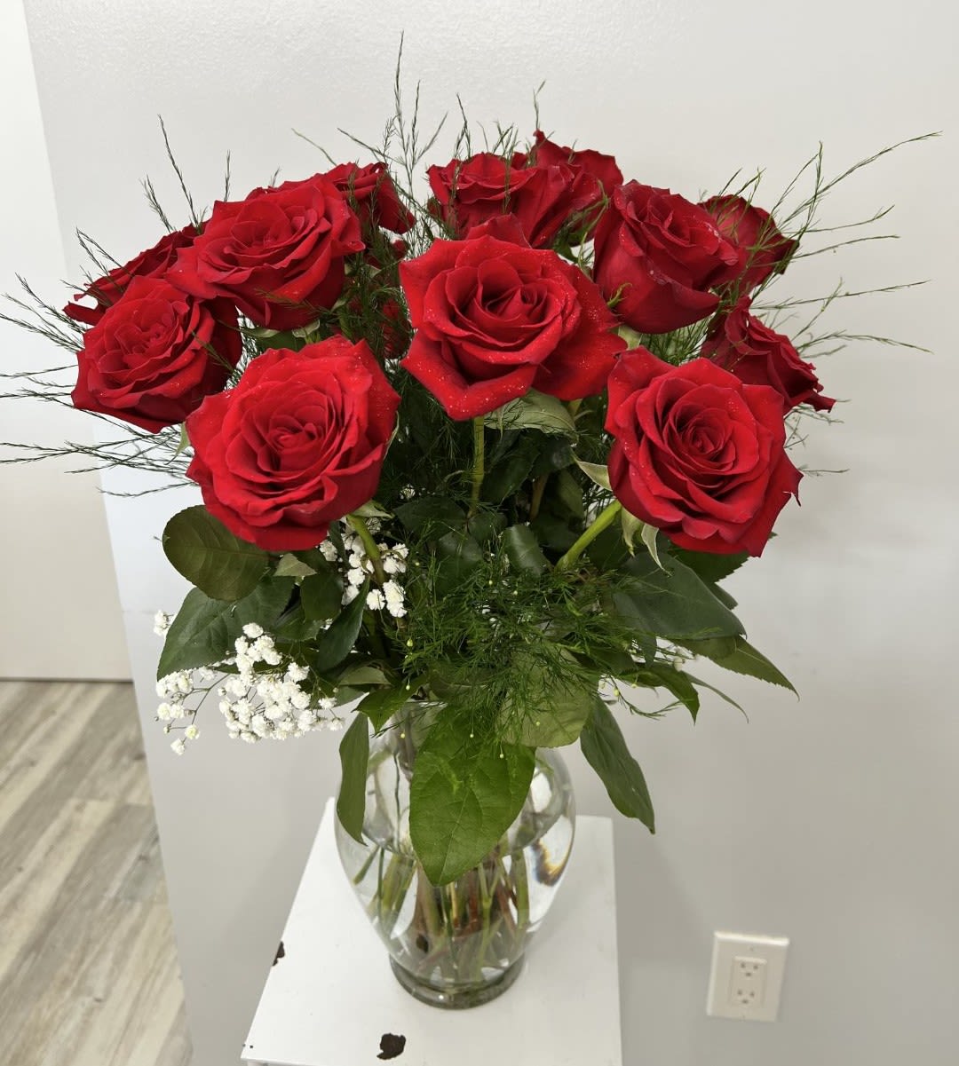 Tall arrangement of red roses with white filler flowers in a clear glass vase