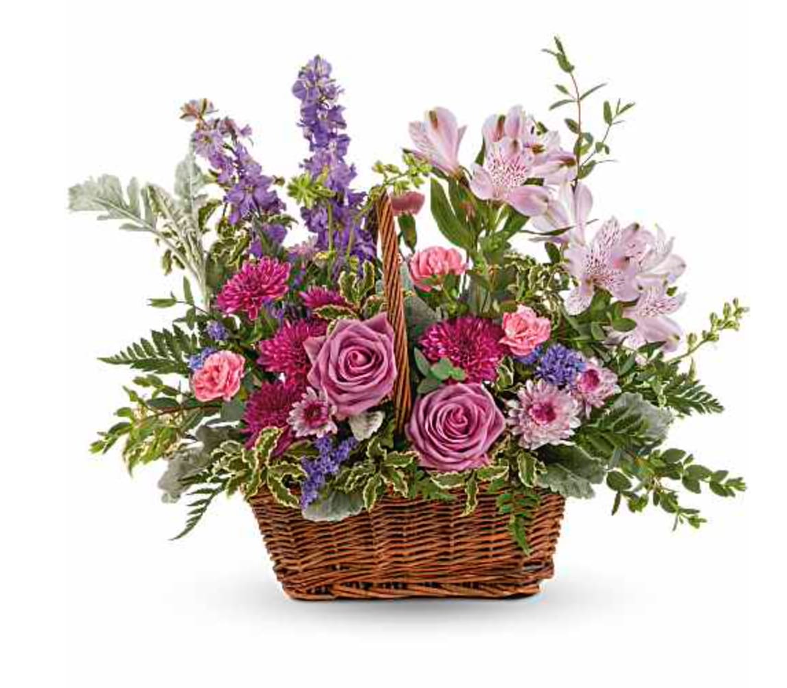 Lavender Meadow Basket Bouquet - This lush lavender rose arrangement is a basket of beauty to brighten any day! This bouquet features lavender roses, lavender alstroemeria, miniature pink carnations, lavender larkspur, purple cushion spray chrysanthemums, lavender button spray chrysanthemums, purple sinuata statice, dusty miller, pitta negra, parvifolia eucalyptus, lemon leaf and leatherleaf fern. Delivered in a Rectangular Basket with Handle. Orientation: One-Sided