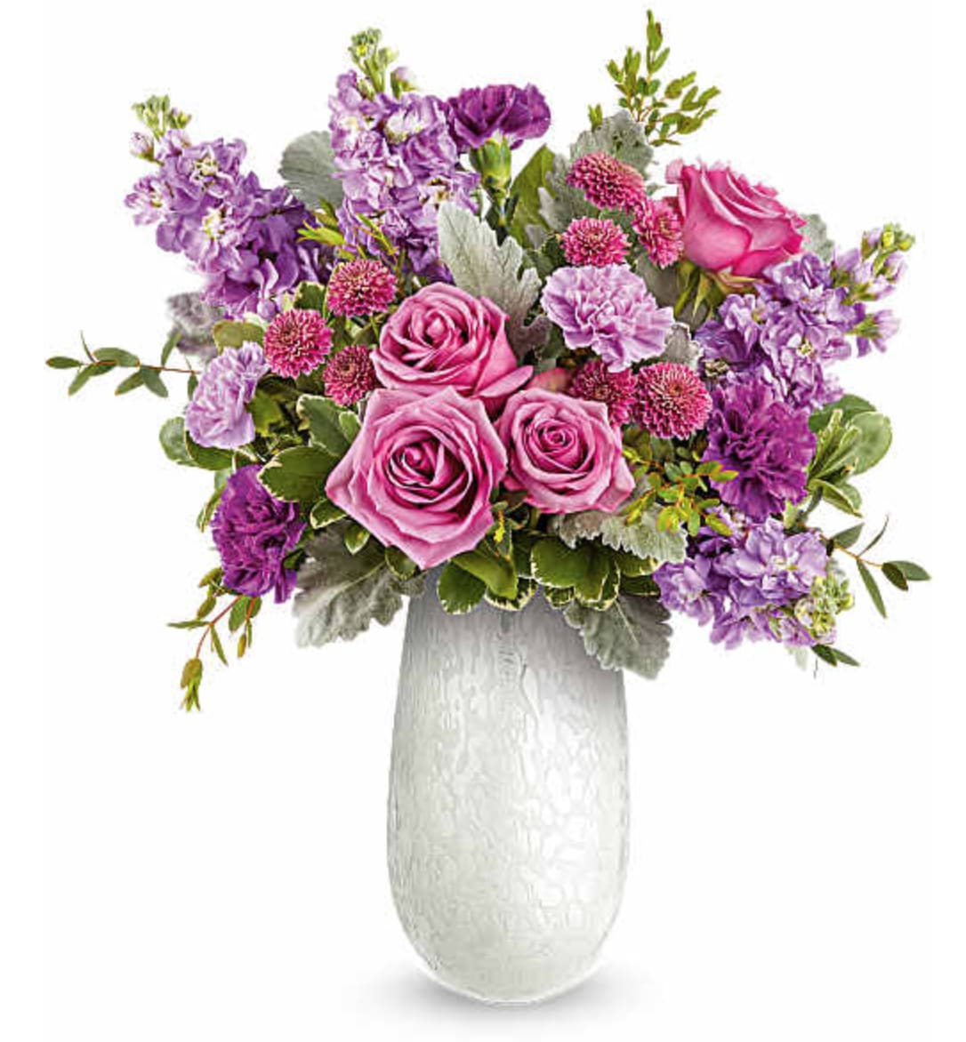 Amelia Bouquet - Delight Mom with our Amelia Bouquet, a graceful mix of pink and lavender blooms beautifully arranged in the Amelia Vase. This elegant art glass keepsake adds soft shimmer and a heartfelt touch to her Mother's Day. The Amelia Bouquet is an elegant Mother's Day floral arrangement featuring lavender roses, lavender and purple carnations, lavender stock, and purple button spray chrysanthemums, accented with dusty miller, parvifolia eucalyptus, and variegated pittosporum, delivered in our Amelia Vase. Orientation: All-Around  SUBSTITUTION POLICY – Always deliver the freshest flowers! Please note the bouquet pictured reflects our original design.  If the exact flowers or container in this arrangement are not available, our local florists will create a beautiful bouquet with the freshest available flowers.