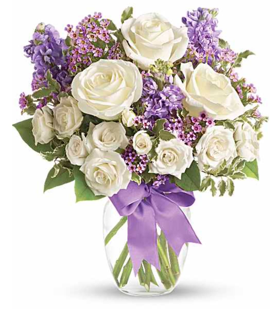 Teleflora's Enchanted Cottage - This magical bouquet will be at home in a cottage, a condo, a studio or an estate. It's so pretty it will be appreciated by all those lucky enough to receive it. Enchant someone today! White roses and spray roses, lavender stock and waxflower, all perfectly arranged in a clear glass vase that's wrapped with purple ribbon.