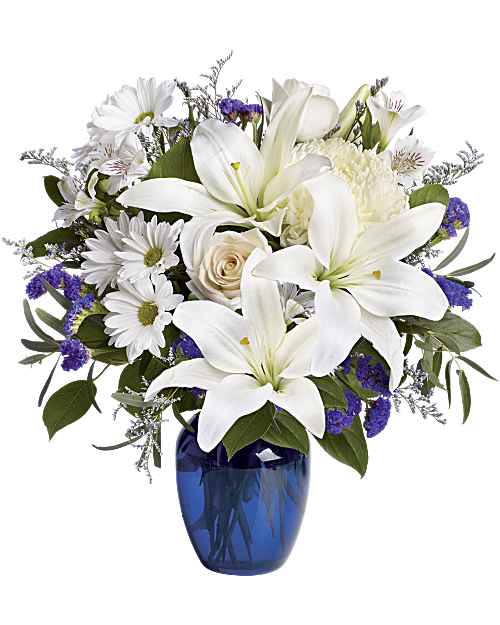 Beautiful in Blue - Brighten the home with the peace and beauty of a bright blue sky. This beautiful bouquet with pure white flowers in a gorgeous blue glass vase. Beautiful blooms such as crème roses, white lilies and alstroemeria along with white chrysanthemums, eucalyptus, limonium and more are beautifully arranged in a dazzling cobalt blue vase. Orientation: One-Sided