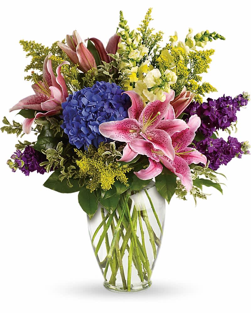 Bouquet of pink lilies, blue hydrangea, and purple flowers in a glass vase