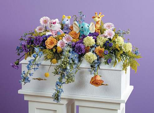 Colorful floral arrangement with plush animals on a white casket