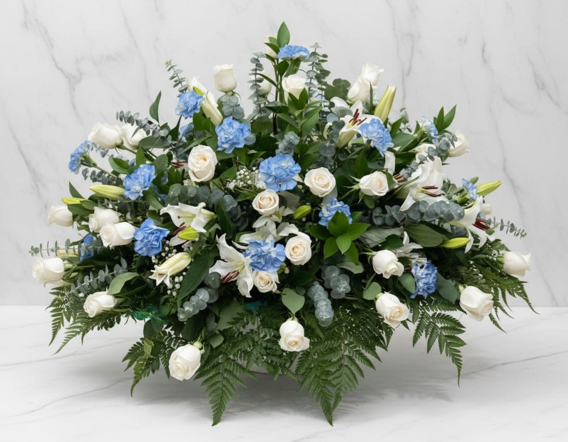 Gentle Sky Tribute - Delicate painted blue carnations are beautifully paired with white roses, white lilies, gysophila, surronded by fresh eucalyptus, fern, and seasonal greenery. For funerals, it express comfort, emphaty, and tranquility. Delicadas claveles pintadas de azul se combinan hermosamente con rosas blancas, lirios blancos, gypsophila, rodeadas de eucalipto fresco, helecho y vegetación de temporada. Para funerales, expresa consuelo, empatía y tranquilidad.
