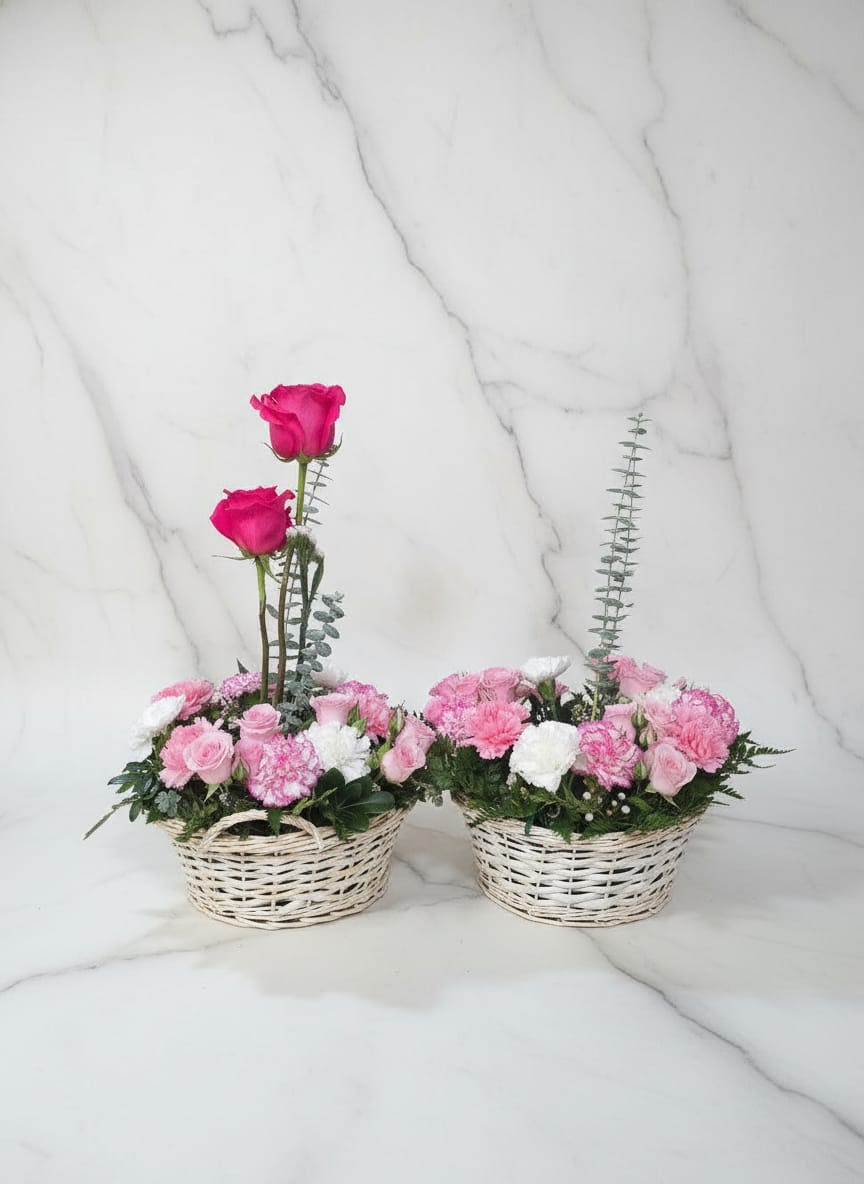 Pink Garden Duo - Each basket showcases beautiful pink roses and pink carnations, accented with touches of gypsophila, and complemented by fresh eucalyptus and seasonal greenery. Two elegant hot pink roses rise above one of the baskets, adding height and a graceful focal point to the arrangement. Some features can change according to the client and disponoble materials. Cada cesta exhibe hermosas rosas rosadas y claveles rosas, acentuadas con toques de gypsophila y complementadas con eucalipto fresco y follaje de temporada. Dos elegantes rosas de color rosa intenso sobresalen de una de las cestas, añadiendo altura y un punto focal elegante al arreglo. Algunos cambios se pueden hacer de acuerdo al cliente y los materiales disponibles.