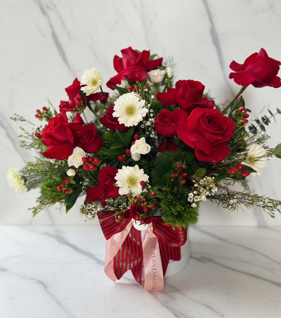 Ruby Rose Garden - This centerpiece features vibrant red roses paired with delicate white daisy, creating a lovely contrast of rich color and soft charm. Accented with decorative red berries and fresh green foliage.  Este centro de mesa presenta vibrantes rosas rojas combinadas con delicadas margaritas blancas, creando un encantador contraste de color intenso y suave encanto. Acentuado con bayas rojas decorativas y follaje verde fresco.