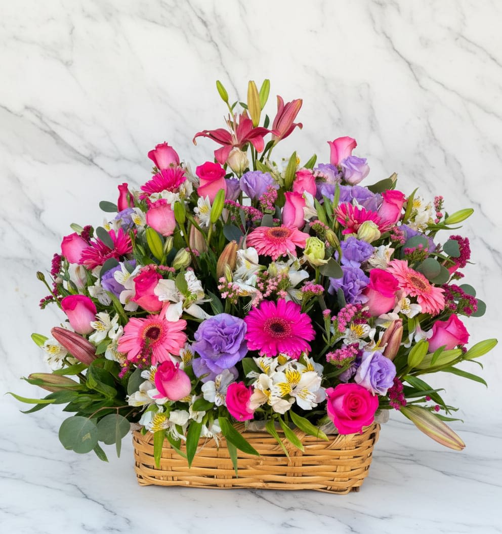 Floral Symphony Basket - A vibrant and soft floral basket filled with a beautiful mix of colorful blooms arranged in a natural garden style. This cheerful arrangement combines soft pink, purple, and white flowers with fresh greenery, creating a lively and refreshing display. Una canasta floral vibrante y suave llena de una hermosa mezcla de flores coloridas dispuestas al estilo de un jardín natural. Este arreglo alegre combina flores suaves de color rosa, púrpura y blanco con vegetación fresca, creando una exhibición animada y refrescante.