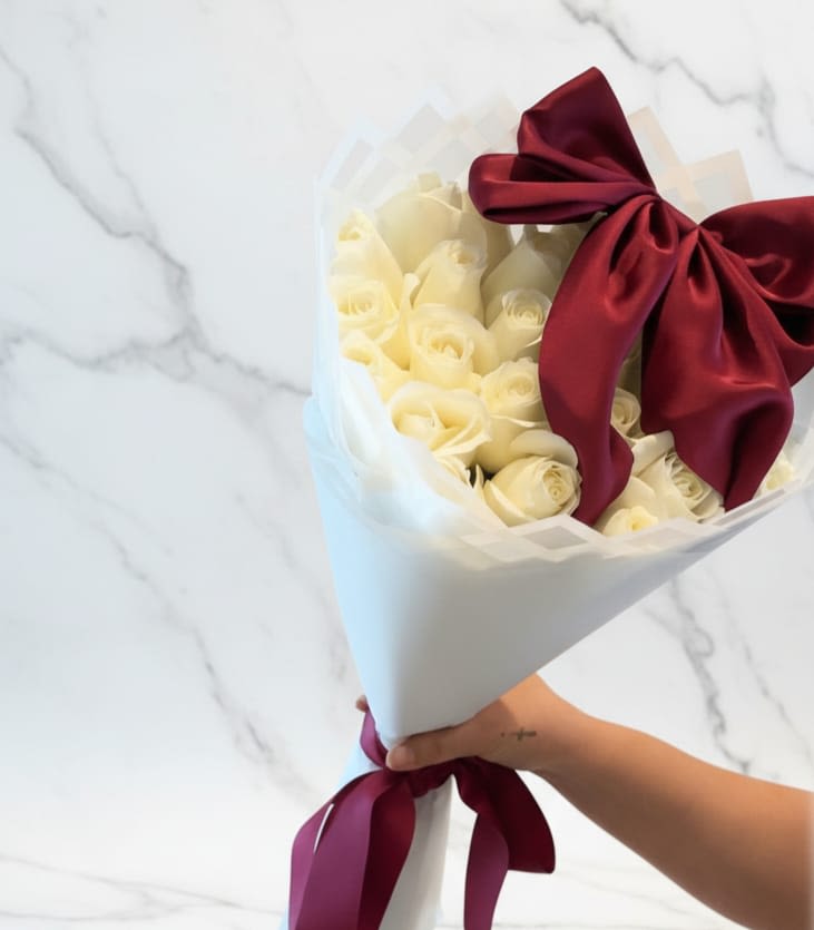 Classic Ivory Bouquet - A refined and elegant bouquet featuring soft white blooms beautifully wrapped in floral paper and finished with a romantic ribbon. The delicate white roses create a timeless and graceful look, while rich riboon adds touch of warmth. Un ramo refinado y elegante con delicadas flores blancas, bellamente envuelto en papel floral y terminado con un lazo romántico. Las delicadas rosas blancas crean un aspecto atemporal y elegante, mientras que el lazo rico aporta un toque de calidez.