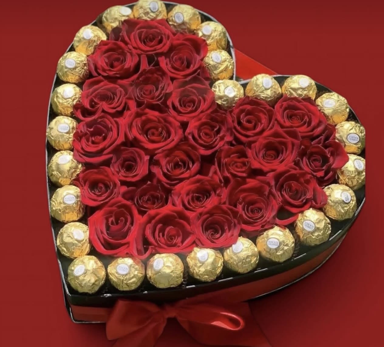 Heart-shaped box of red roses surrounded by gold-wrapped chocolates