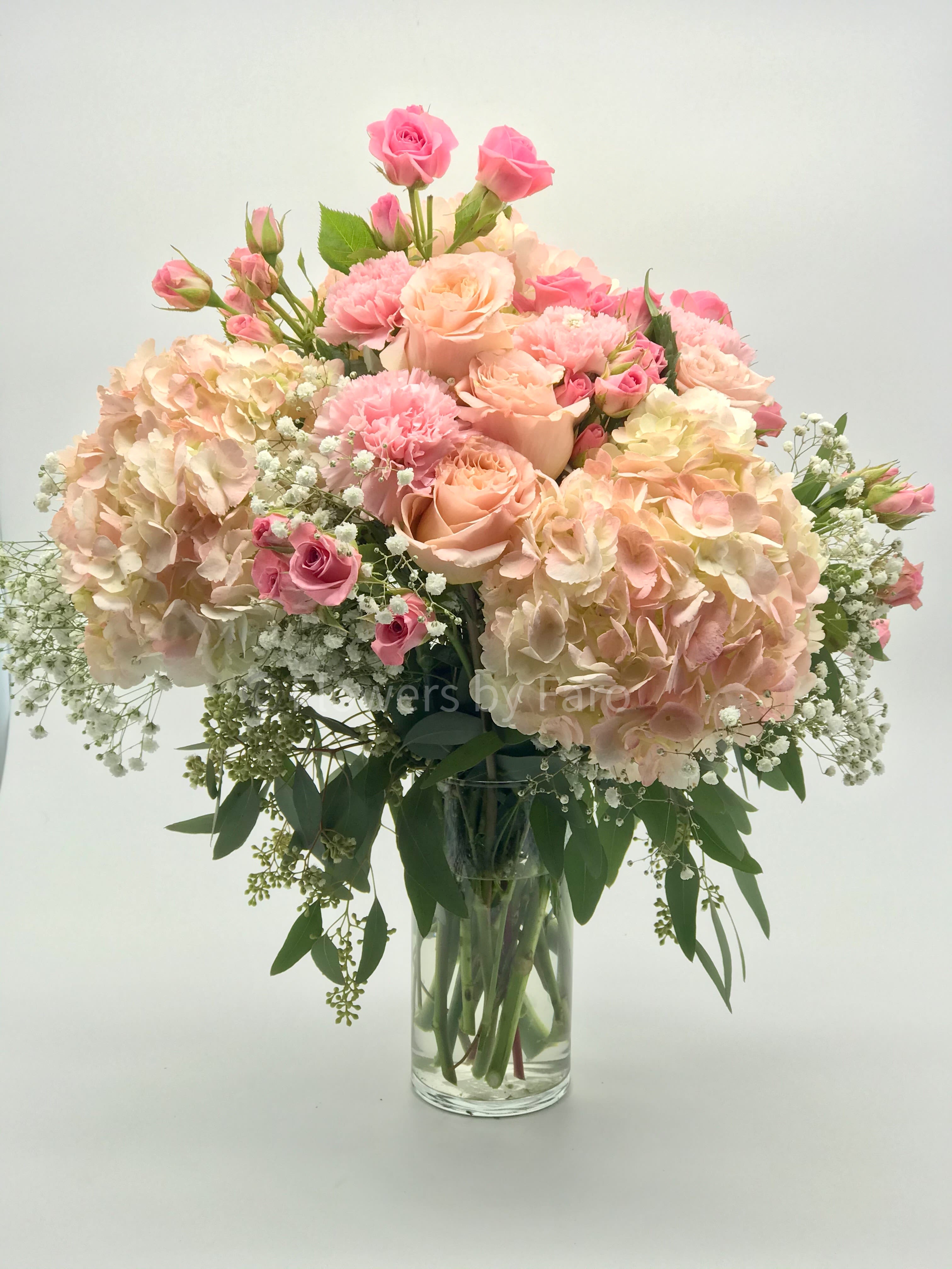 Tall glass vase of blush hydrangeas, pink roses, carnations, and baby’s breath in a soft pastel arrangement