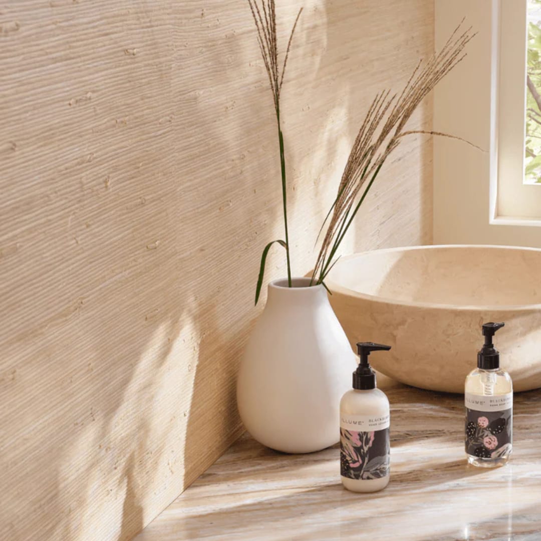 White vase with tall dried grass stems beside two pump bottles