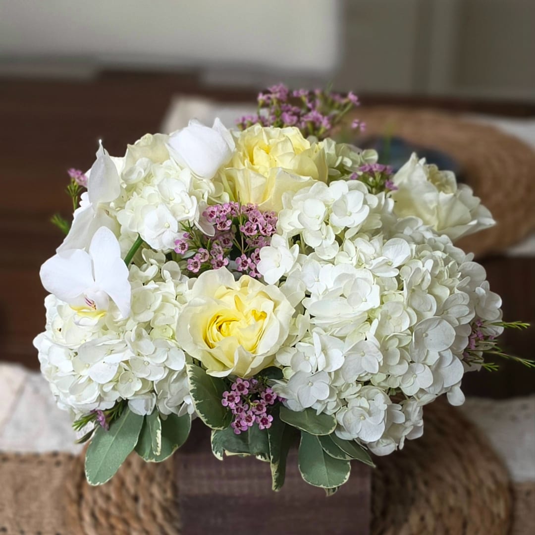 White hydrangea and pale yellow roses in a square vase with small pink accents