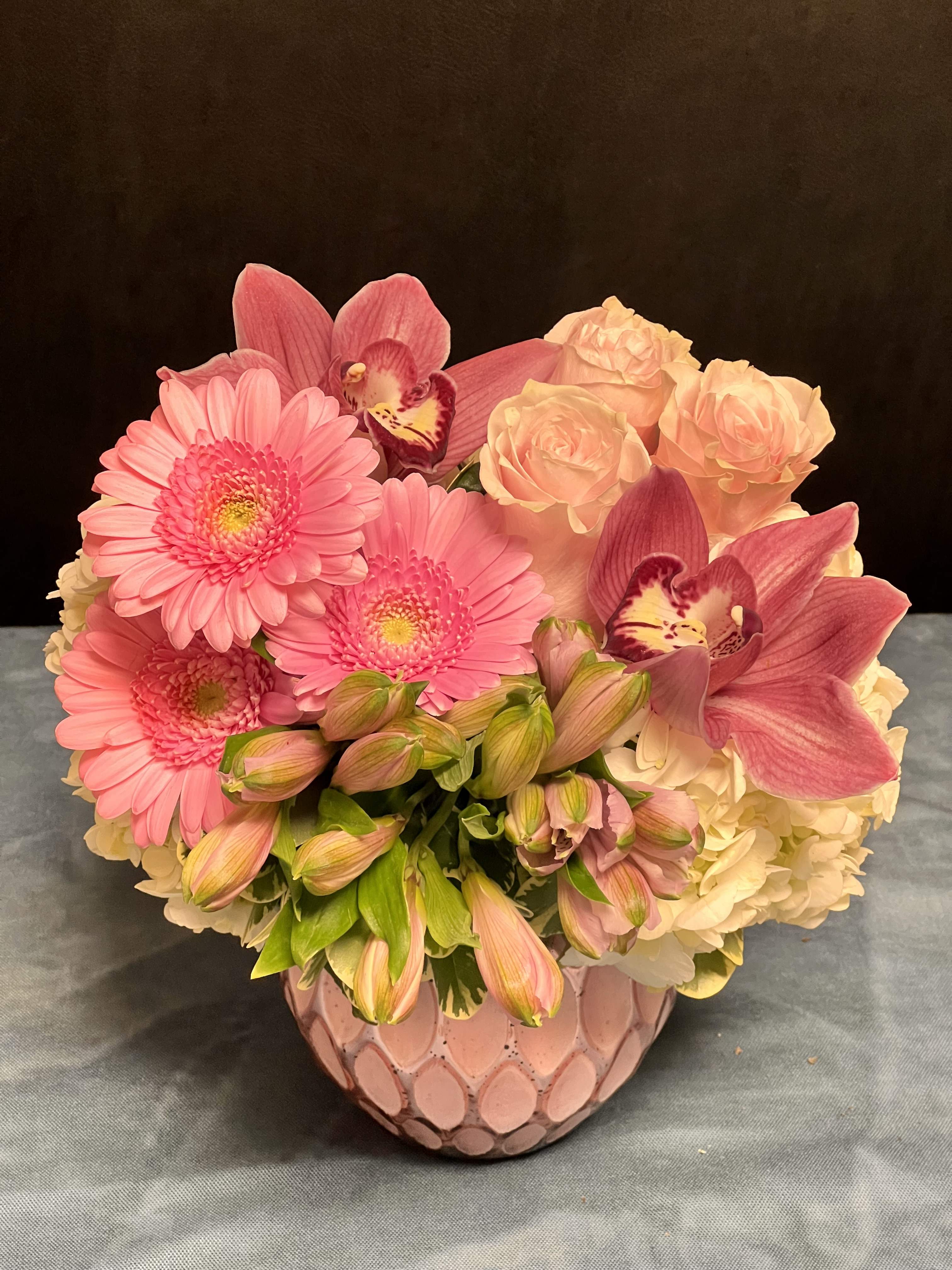 Pink Passion - A romantic medley of soft and striking pinks, this lush arrangement speaks the language of love and grace. Featuring delicate pink roses, cheerful pink gerbera daisies, airy pink alstroemerias, and exotic pink cymbidium orchids, all nestled against the cloud-like backdrop of white hydrangeas. A timeless expression of femininity, warmth, and heartfelt emotion.