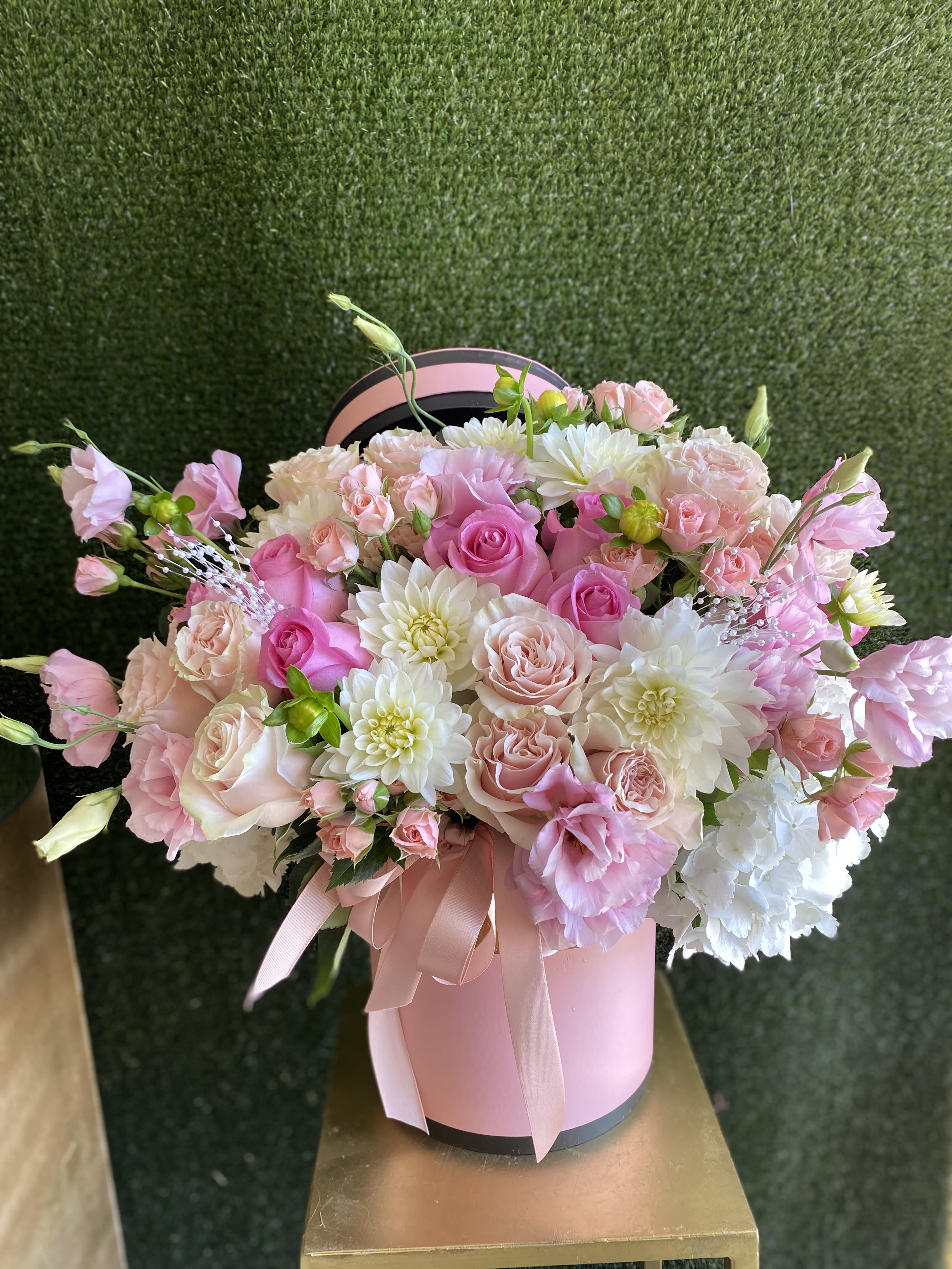 Pink and white roses with white blooms in a pink hatbox tied with ribbon