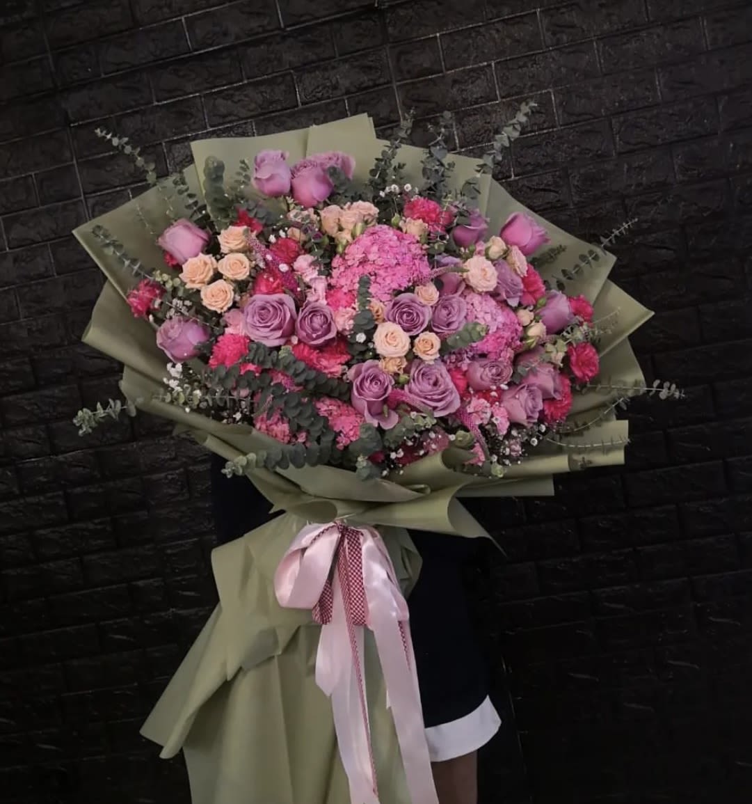 Large bouquet of pink and lavender roses with mixed blooms wrapped in olive paper
