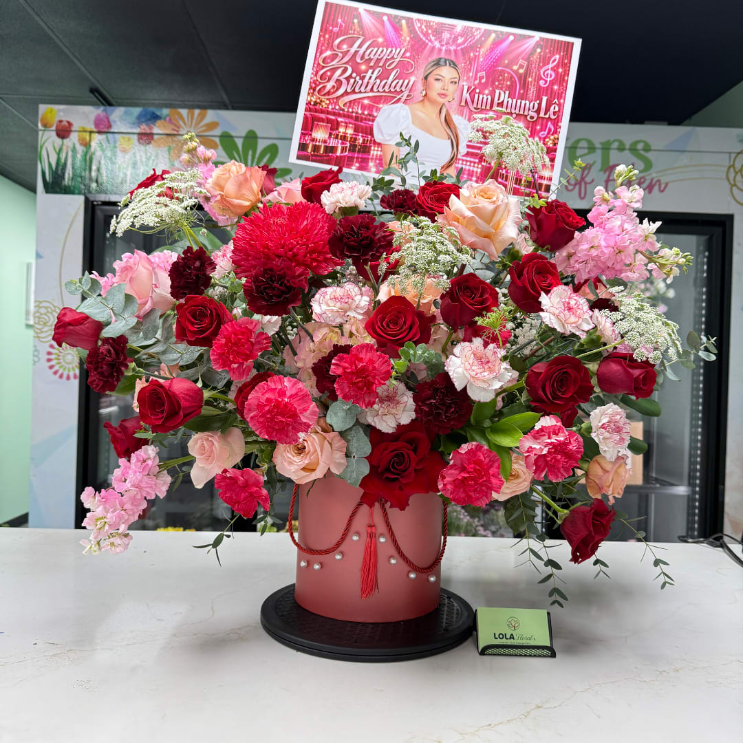 Large mixed bouquet of red, pink, and peach flowers in a pink box